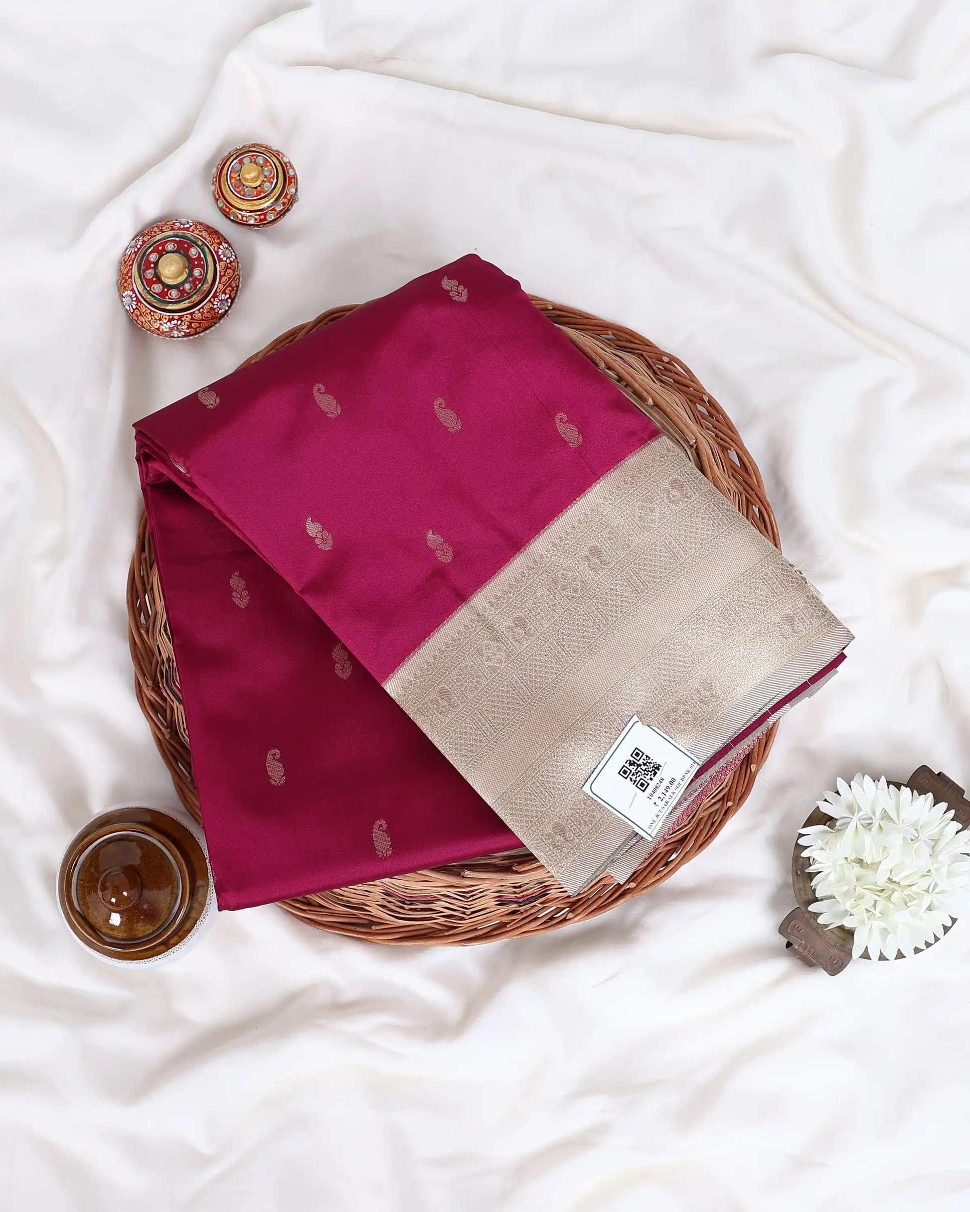 A folded magenta and beige silk saree with small gold motifs, displayed on a woven tray 