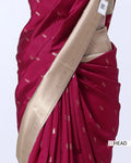 A close-up of a draped saree in deep magenta with small metallic motifs and a wide beige border