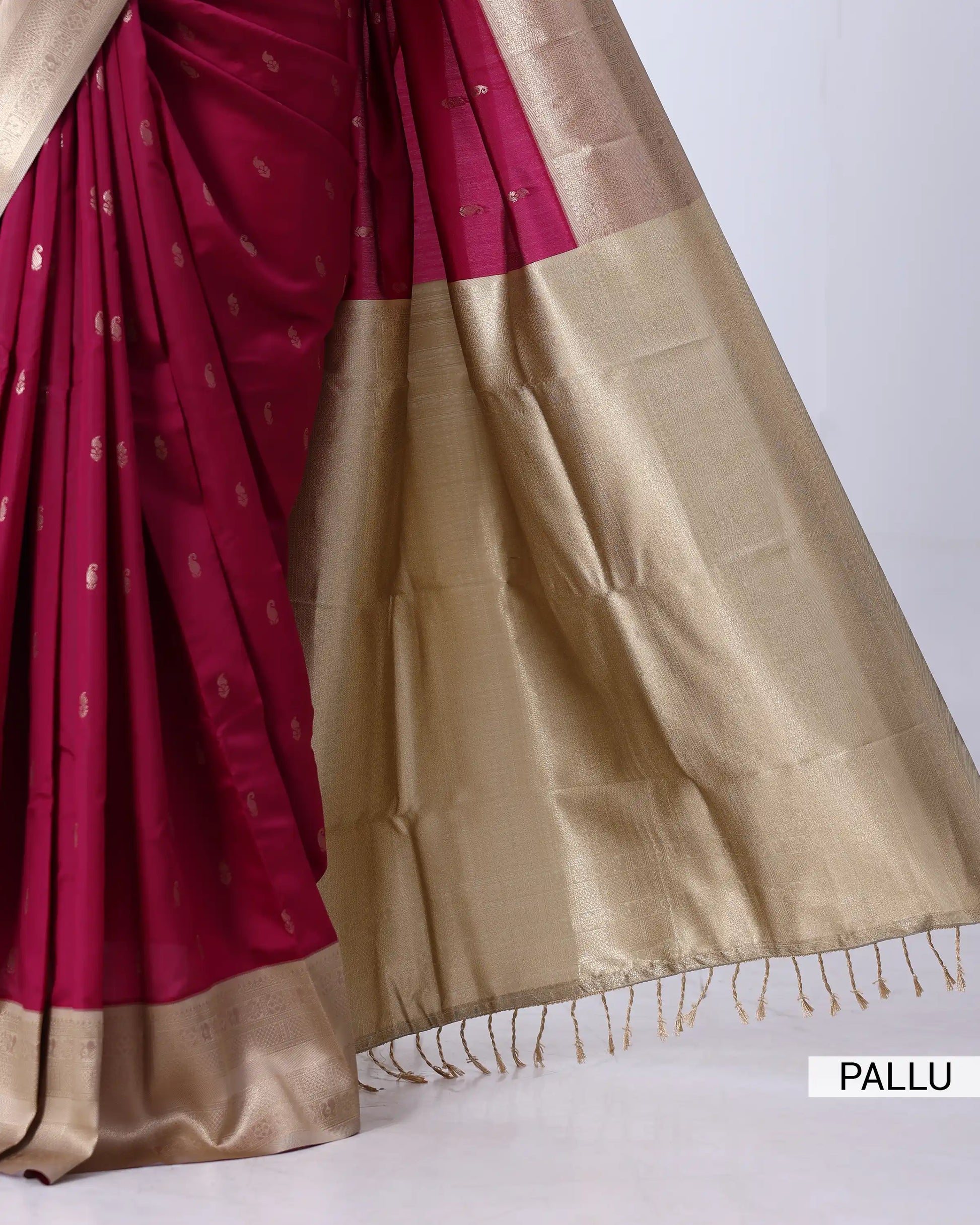 A close-up of a silk saree with a deep magenta body, small gold motifs, and a wide shimmering gold pallu border
