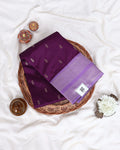 A folded purple silk saree with small metallic motifs and a lighter purple border