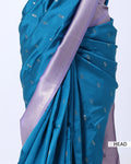 A close-up of a teal blue saree with small silver motifs and a lavender-purple border