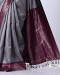 A close-up of a traditional Indian saree, showing the silver-gray body fabric, the deep maroon border, and the metallic gold zari woven patterns.