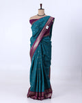 A teal blue-green silk saree with a deep purple border and pallu, decorated with small metallic gold motifs