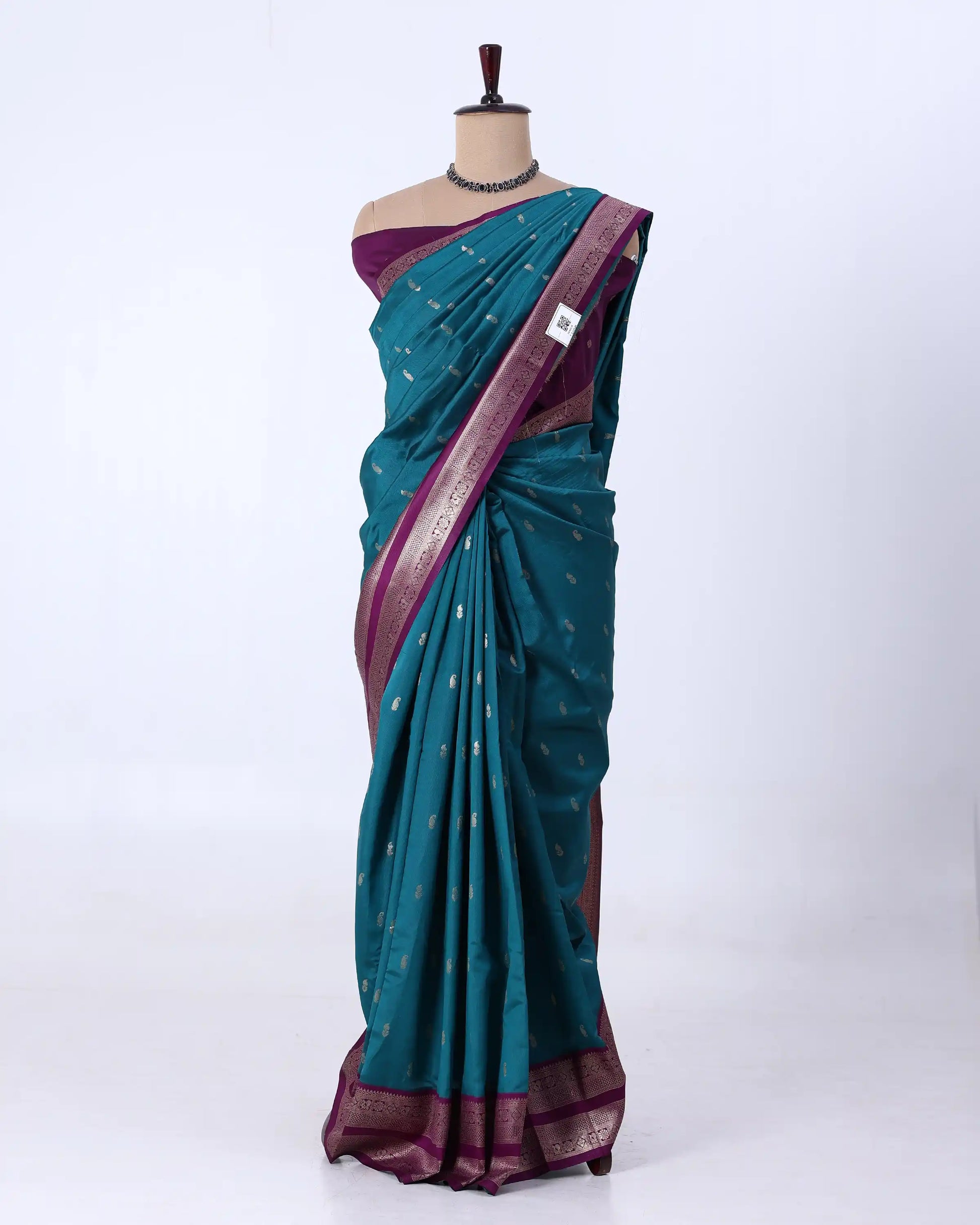 A teal blue-green silk saree with a deep purple border and pallu, decorated with small metallic gold motifs