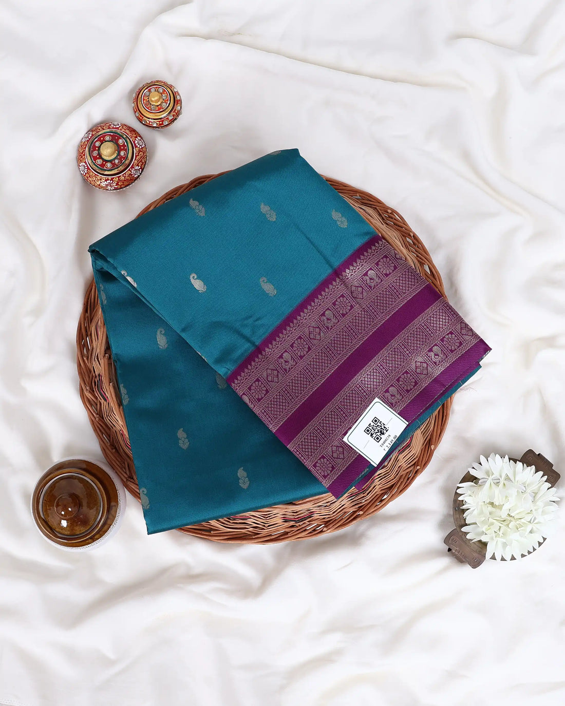 A teal blue-green silk saree with a deep purple border and pallu, decorated with small metallic gold motifs