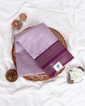 A folded lavender purple silk saree with a deep magenta border and gold motifs