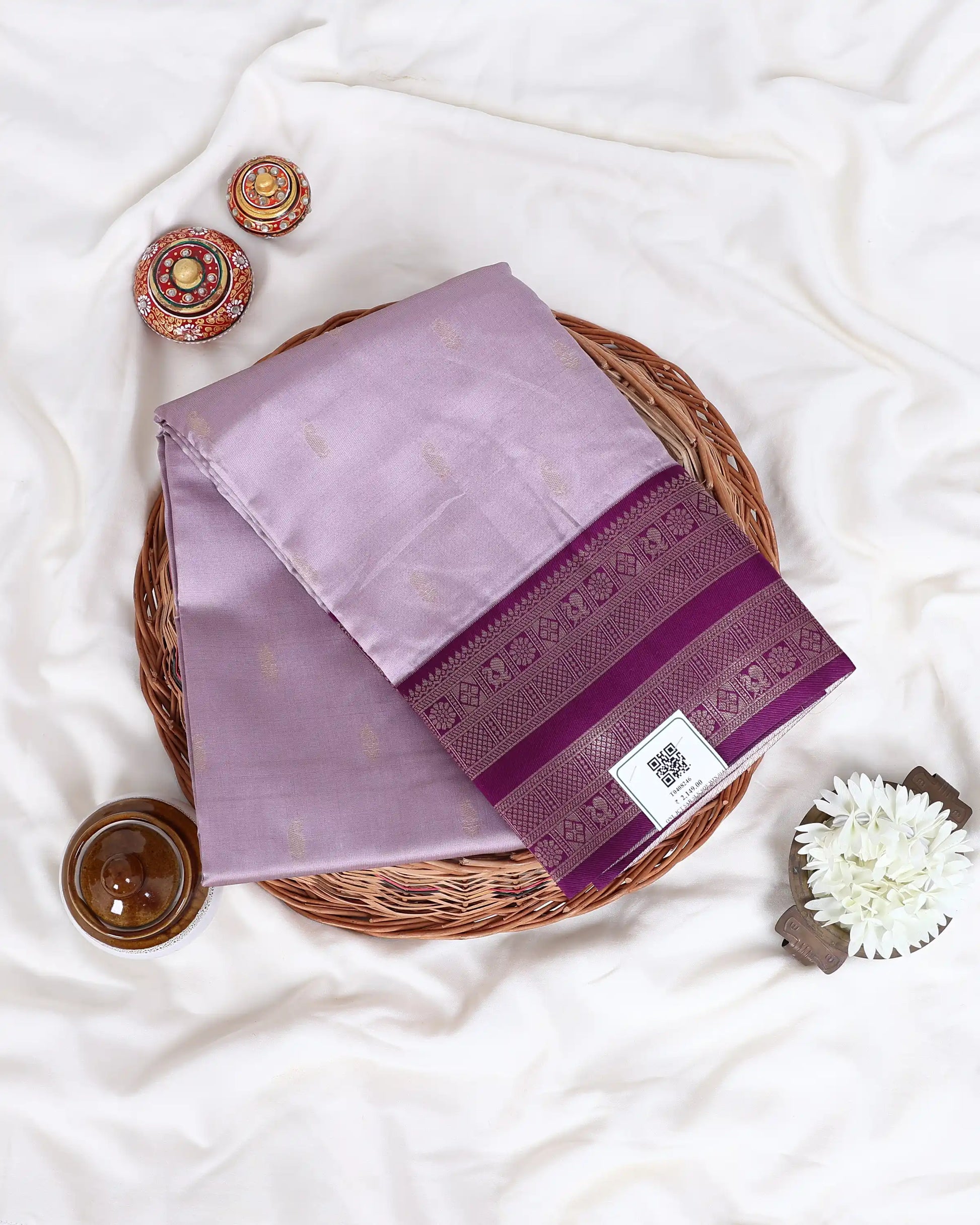 A folded lavender purple silk saree with a deep magenta border and gold motifs
