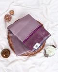 A folded purple silk saree with a detailed brocade border 