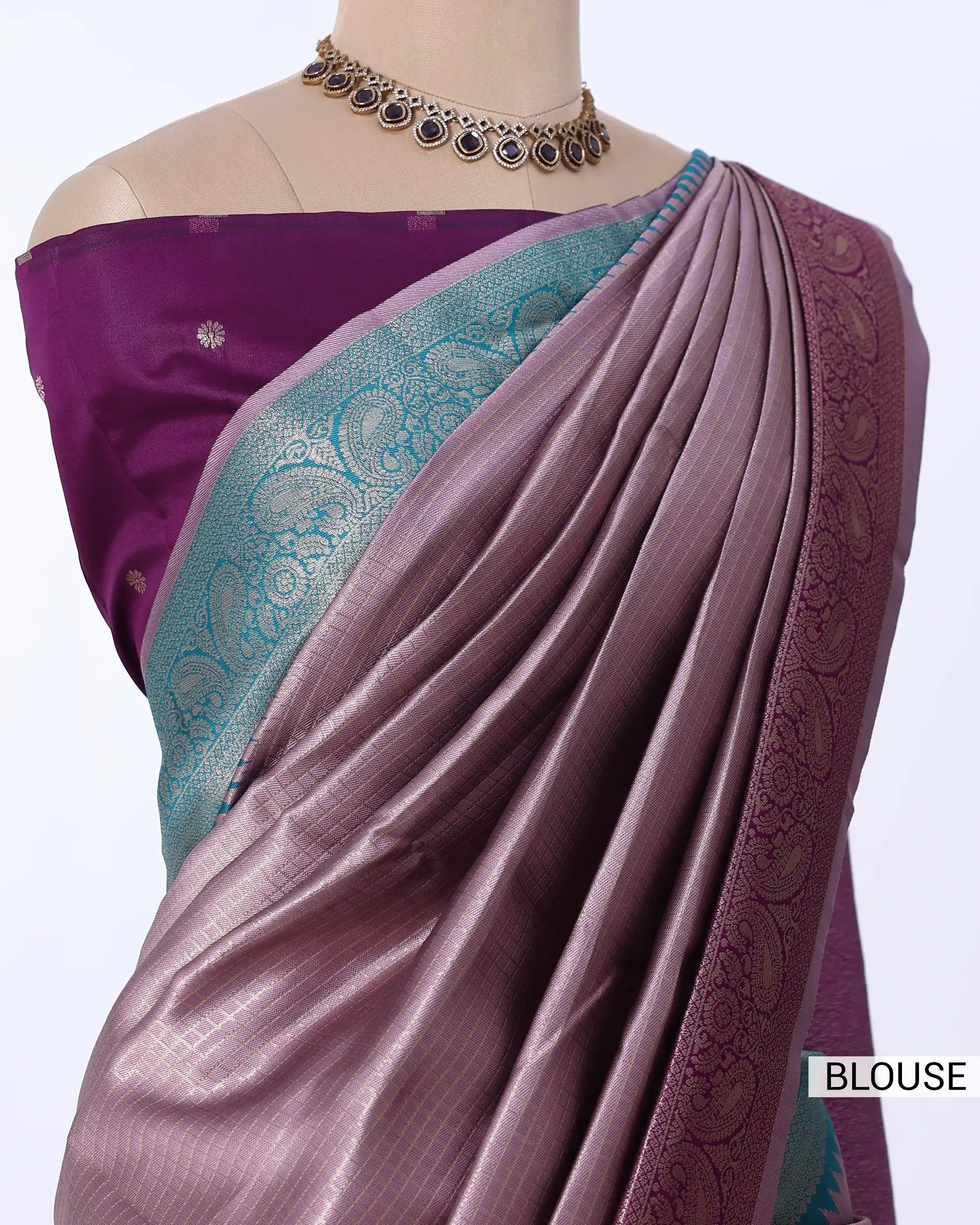 A draped purple saree with a teal and gold patterned border, paired with a matching purple blouse