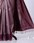 A close-up of a draped purple saree with a metallic sheen, showing the body fabric, pallu end with tassels, and woven pattern 