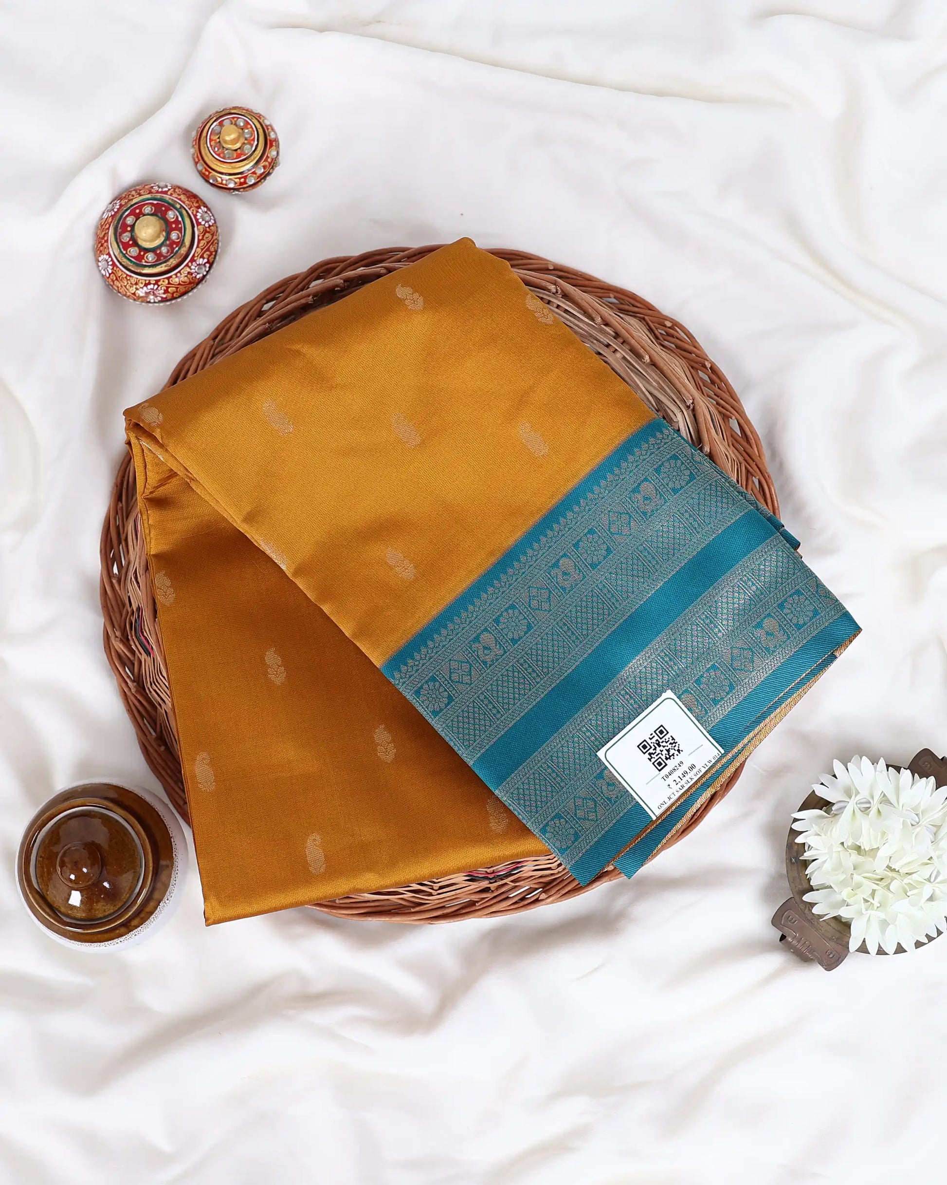 A folded mustard yellow silk saree with a teal blue border and subtle zari motifs