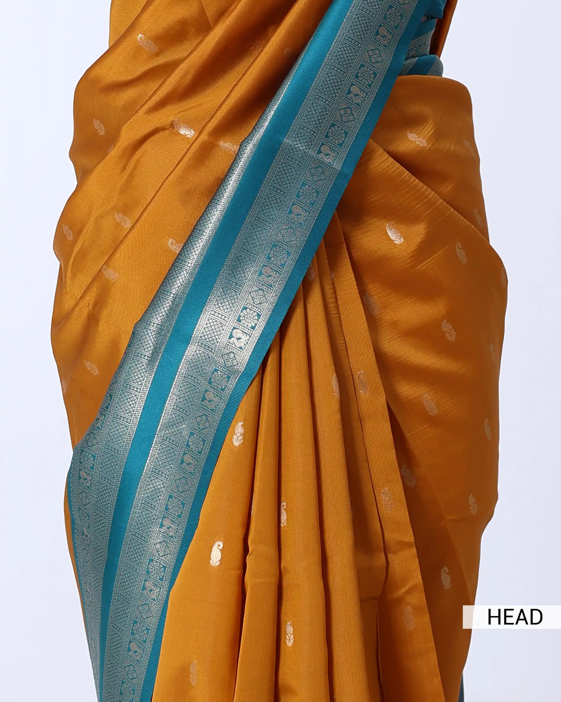 A close-up of a mustard yellow or orange saree with small metallic motifs and a wide turquoise blue border with silver zari detailing