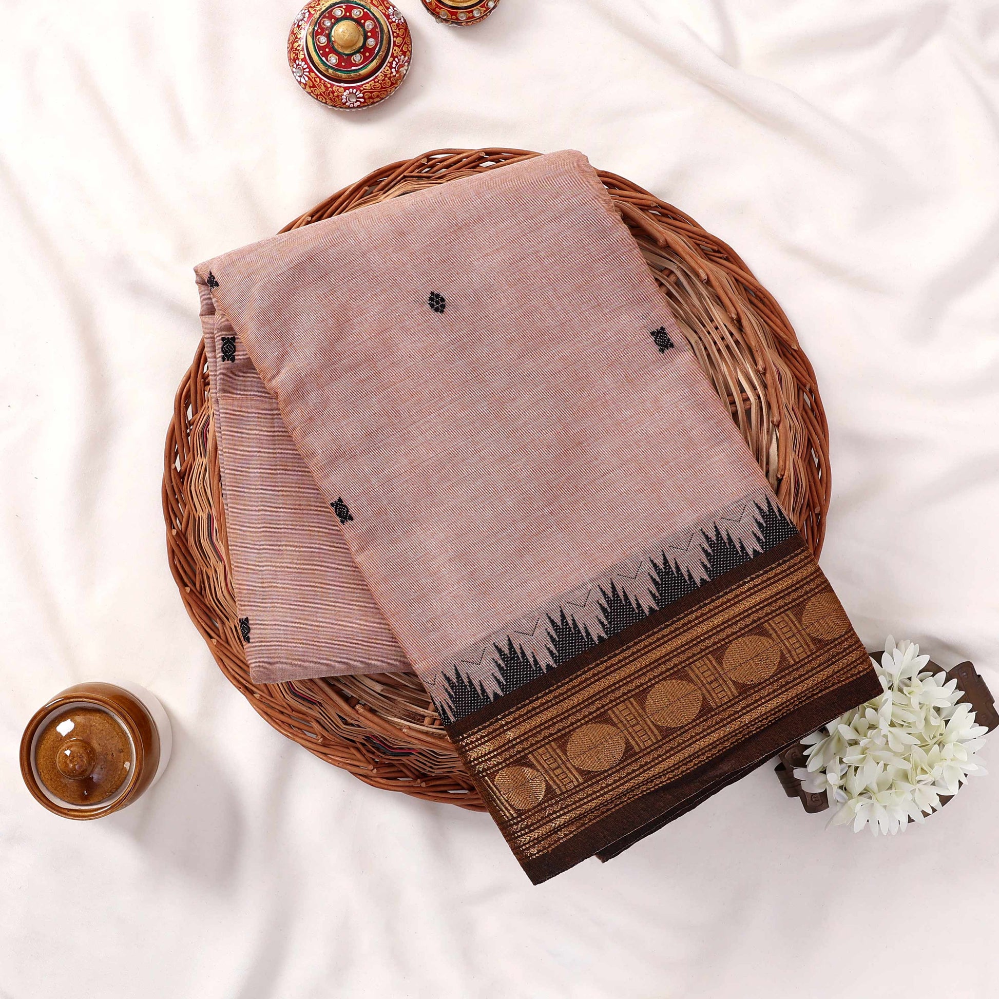 Kanchi Cotton Saree With Zari Border In Beige Color And Black Motifs Folded Flat Lay View With Decorative Accents
