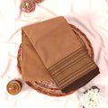 Kanchi Cotton Saree With Gold Zari Border In Beige Tone Folded Flat Lay View On Wicker Basket With Floral Accents

