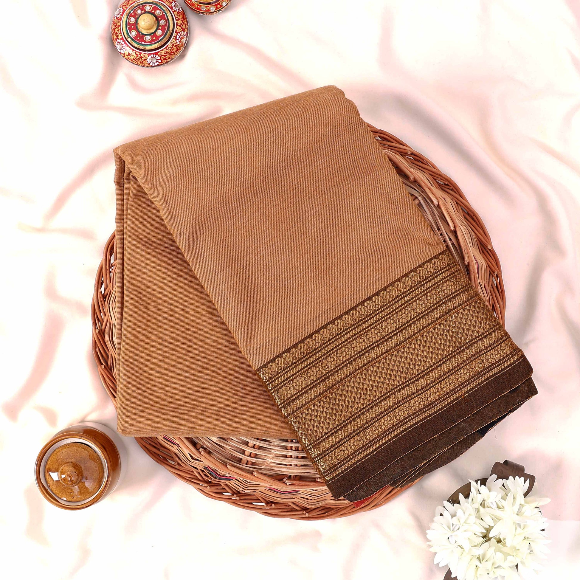 Kanchi Cotton Saree With Gold Zari Border In Beige Tone Folded Flat Lay View On Wicker Basket With Floral Accents
