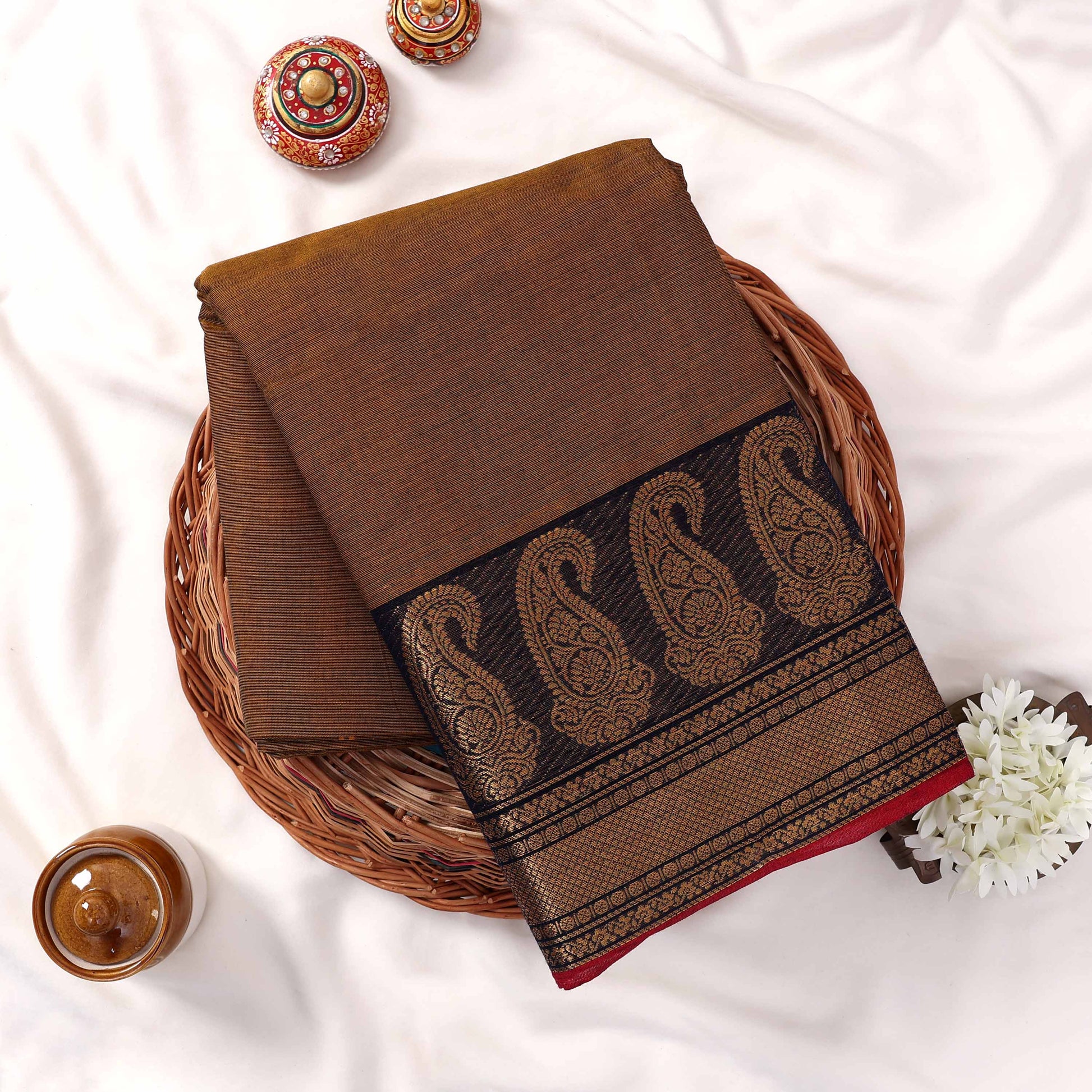Kanchi Cotton Saree With Black And Gold Paisley Border Brown Body Folded Flat Lay View On Woven Basket
