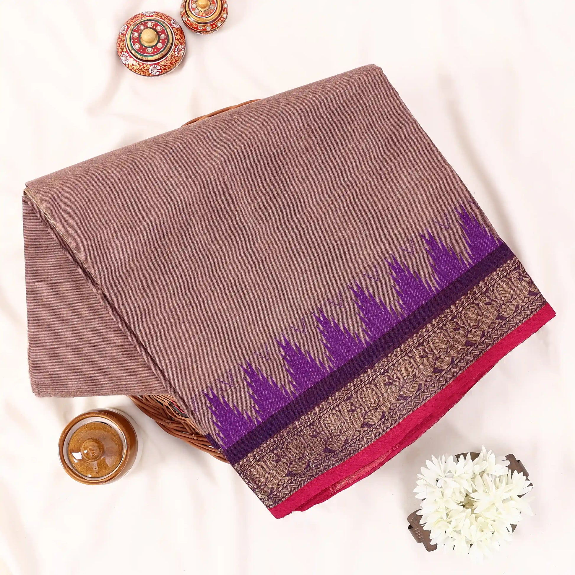 Chettinad cotton saree with subtle brown body purple temple border and zari woven edge folded front view on display.