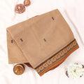 Chettinad cotton saree with beige body black buttas and brown peacock zari border folded in a basket top view.