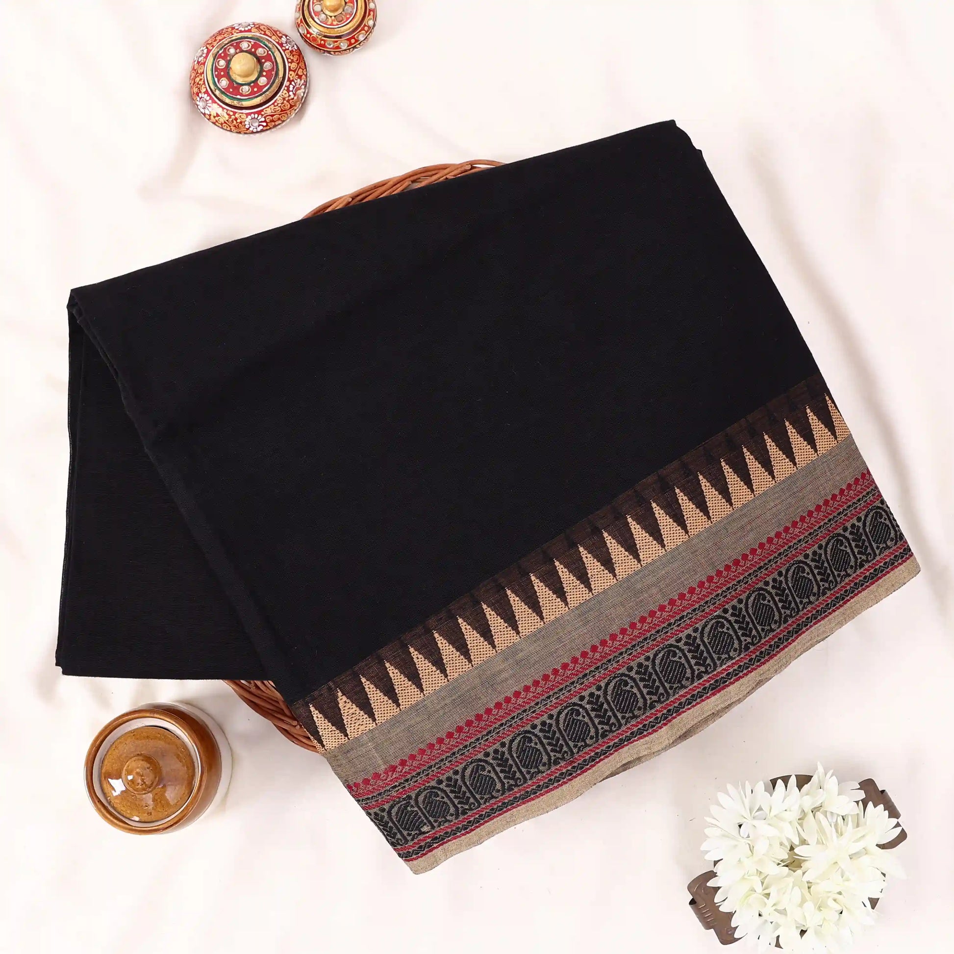 Chettinad cotton saree with solid black body beige temple border and traditional woven zari design folded front view.