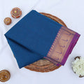 Chettinad cotton saree with blue body and purple zari border folded top view with woven motifs.