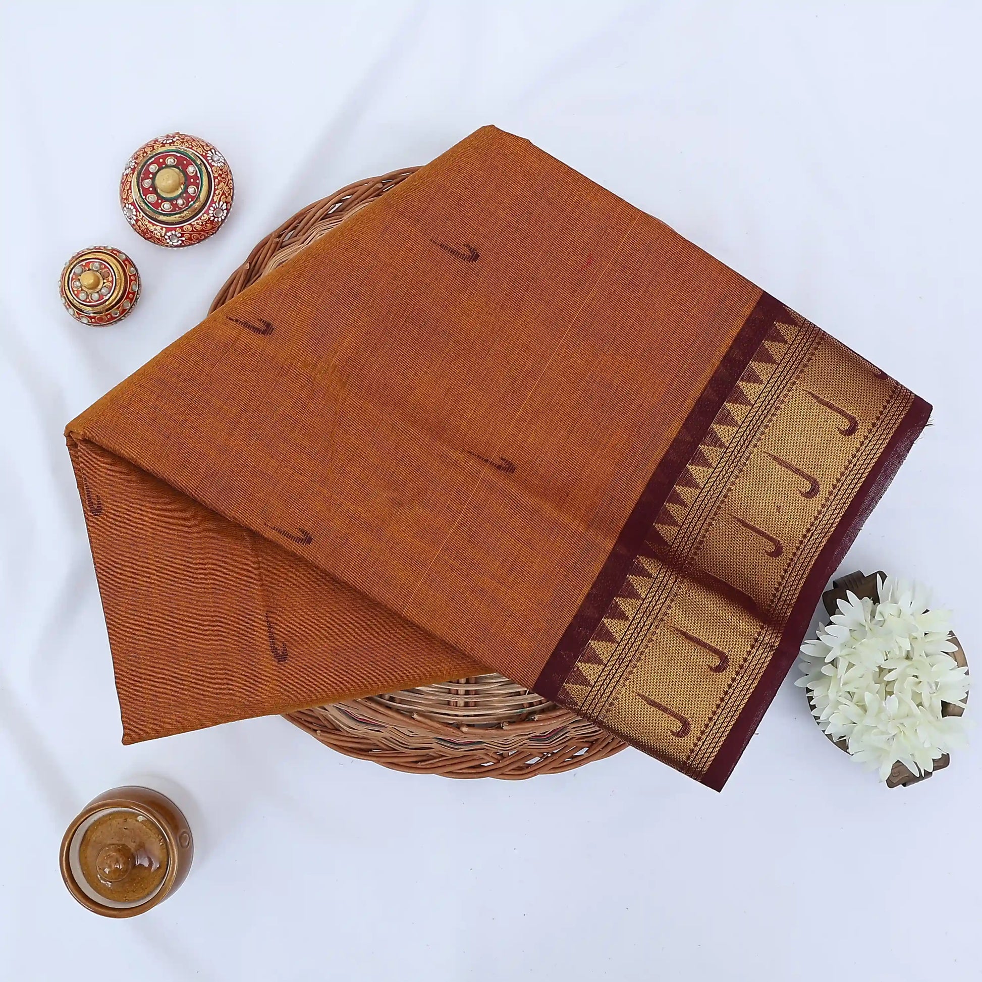 Chettinad cotton saree with brown body and maroon zari border folded top view with woven motifs.
