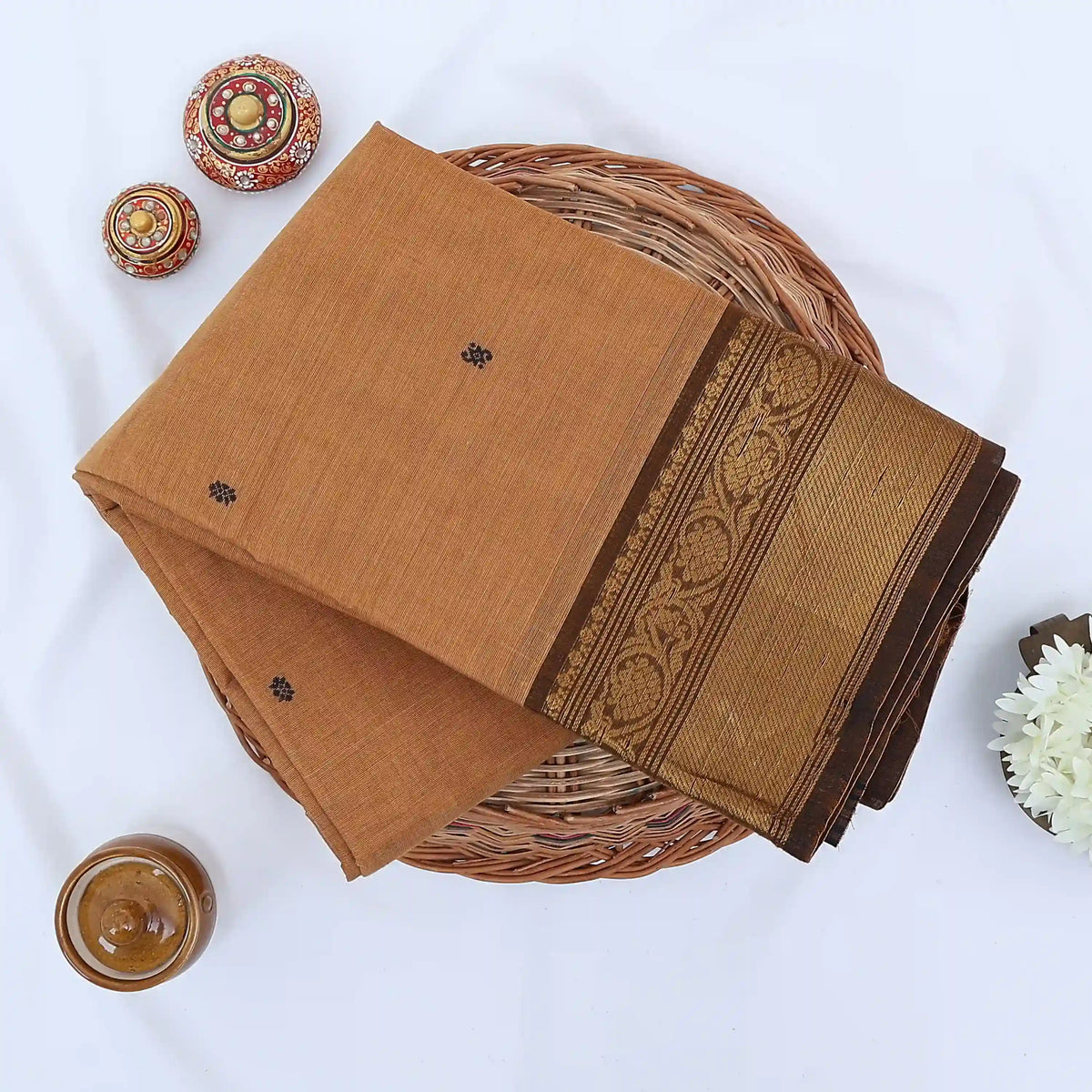 Chettinad cotton saree with beige body black buttas and gold zari border folded in a basket top view.
