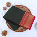 Chettinad cotton saree with dark green body pink buttas and gold zari border folded in a basket top view.
