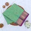 Chettinad cotton saree with green body and purple zari border folded top view with woven motifs.