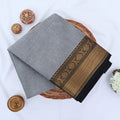 Chettinad cotton saree with grey body black buttas and gold zari border folded in a basket top view.