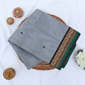 Chettinad cotton saree with grey body black buttas and black peacock zari border folded in a basket top view.