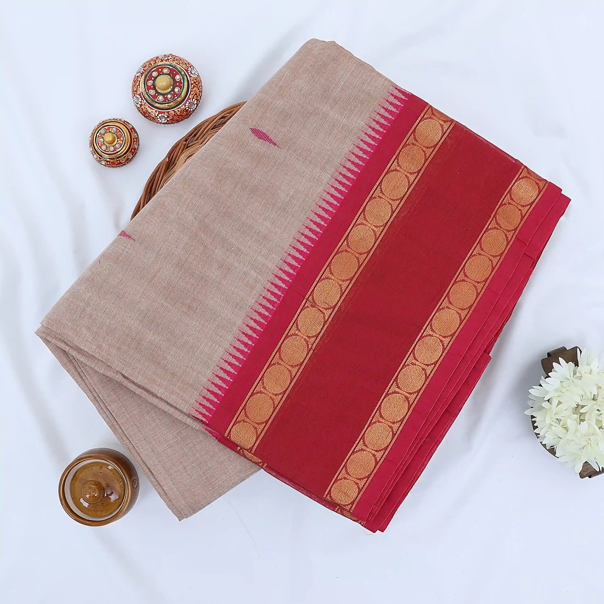 Chettinad cotton saree with plain light brown body red zari border folded top view on wicker basket
