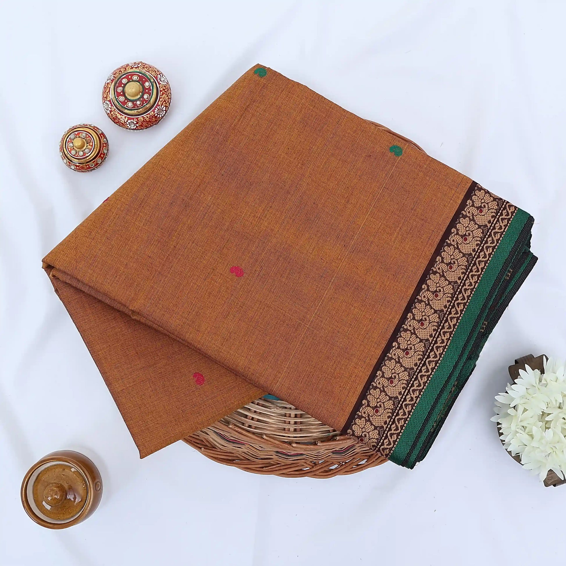 Chettinad cotton saree with brown body multi buttas and black peacock zari border folded in a basket top view.