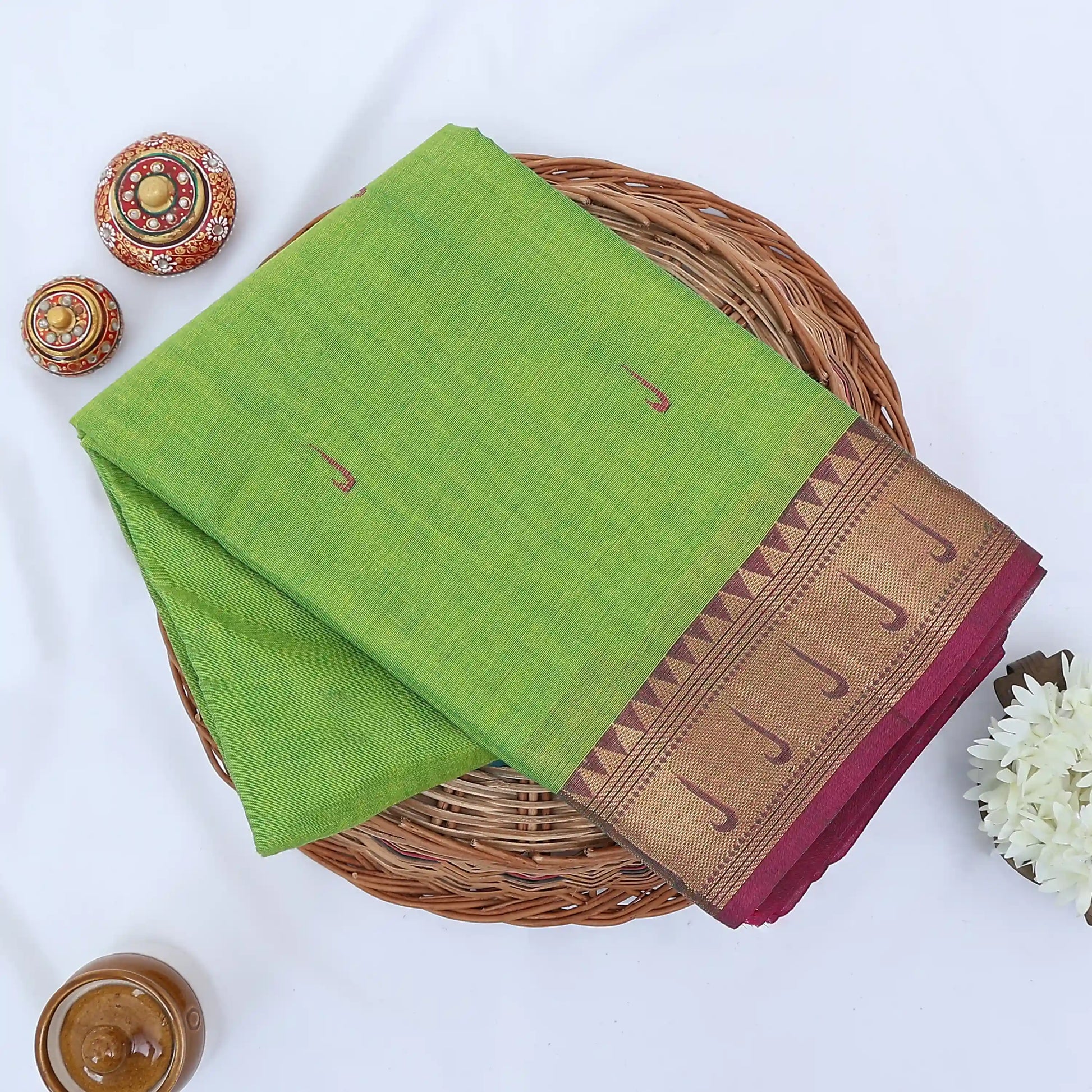 Chettinad cotton saree with light green body and pink zari border folded top view with woven motifs.