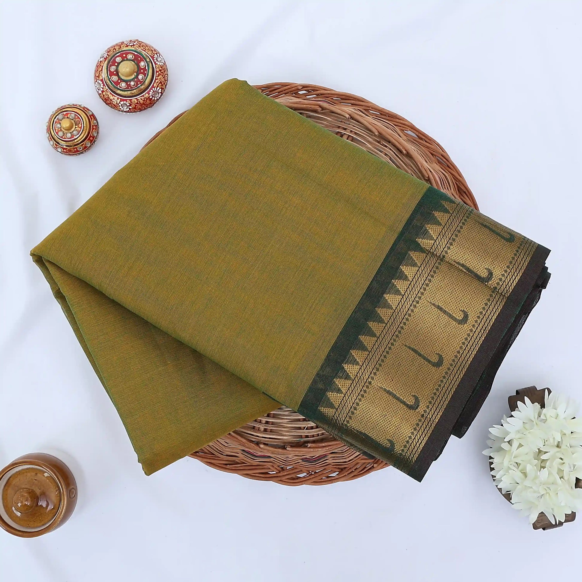 Chettinad cotton saree with olive body and green zari border folded top view with woven motifs.
