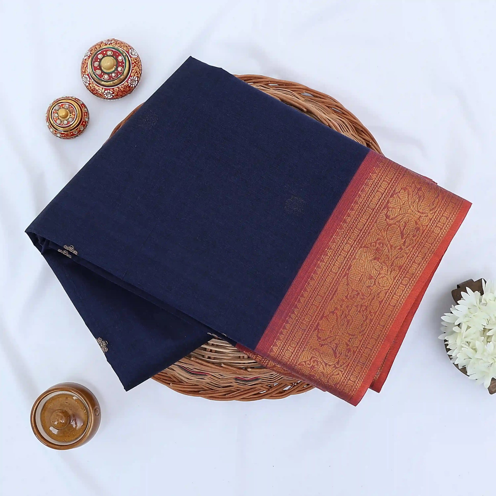 Chettinad cotton saree with zari buttas and floral zari border in navy blue and red folded top view.