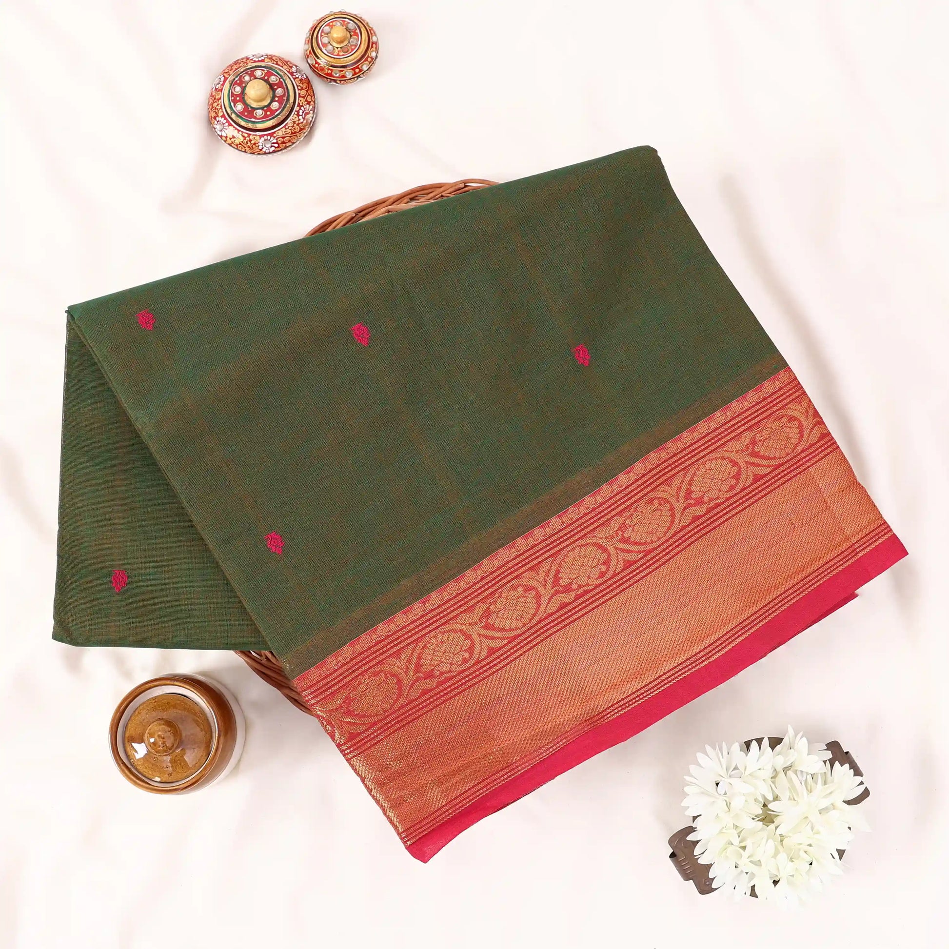 Chettinad cotton saree with olive green body pink buttas and gold zari border folded in a basket top view.