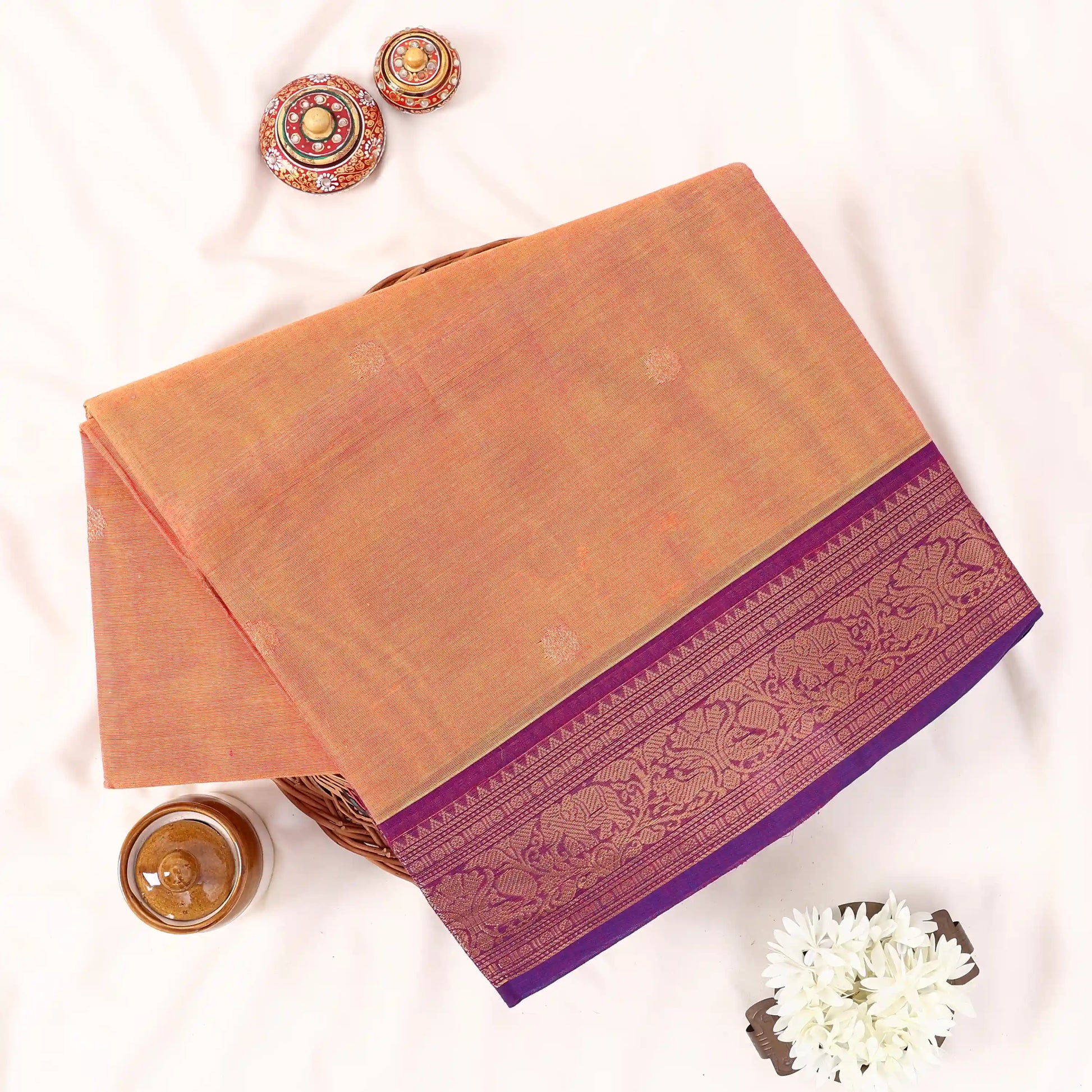 Chettinad cotton saree with zari buttas and floral zari border in orange and purple folded top view.