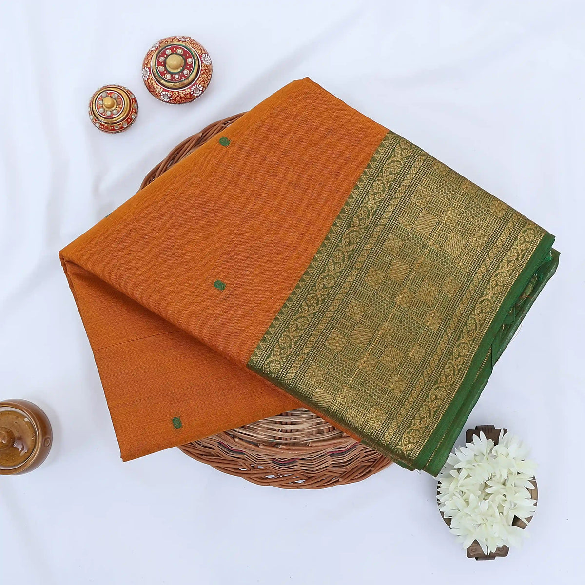 Chettinad cotton saree with plain orange body checked zari border and woven butta motifs folded top view.