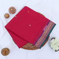 Chettinad cotton saree with pink body multi buttas and purple peacock zari border folded in a basket top view.