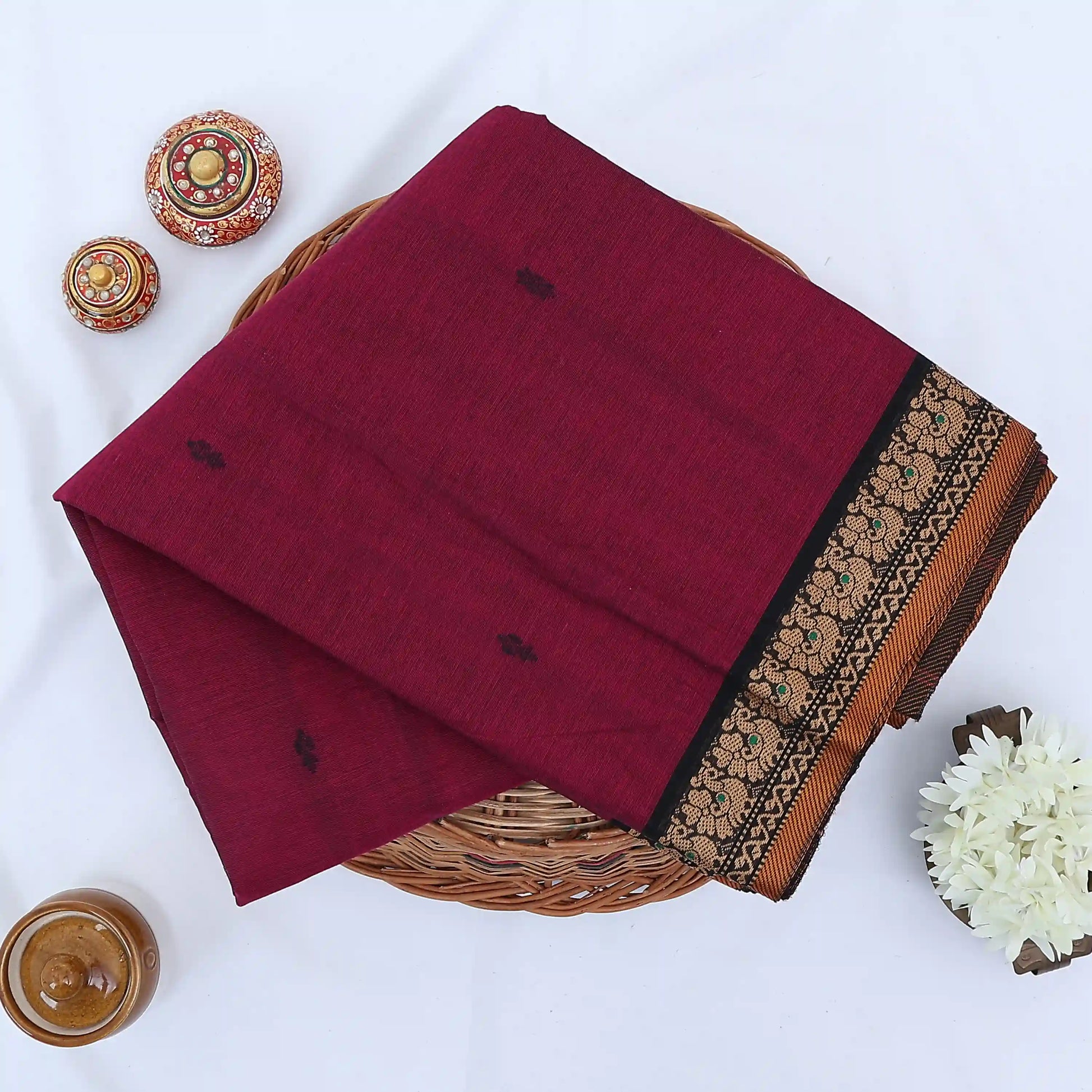 Chettinad cotton saree with purple body black buttas and black peacock zari border folded in a basket top view.