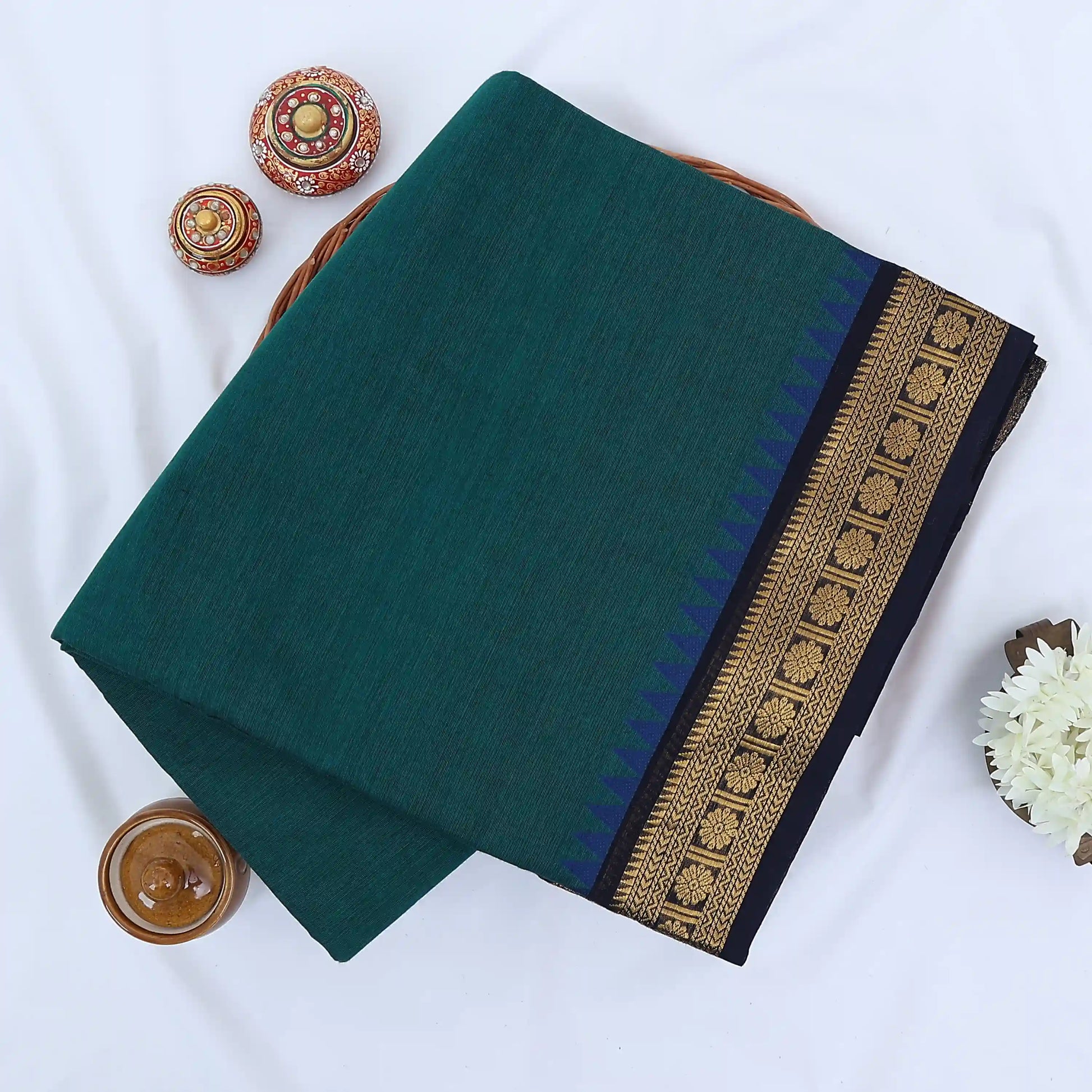 Chettinad cotton saree with plain teal green body gold zari floral border folded top view on wicker basket