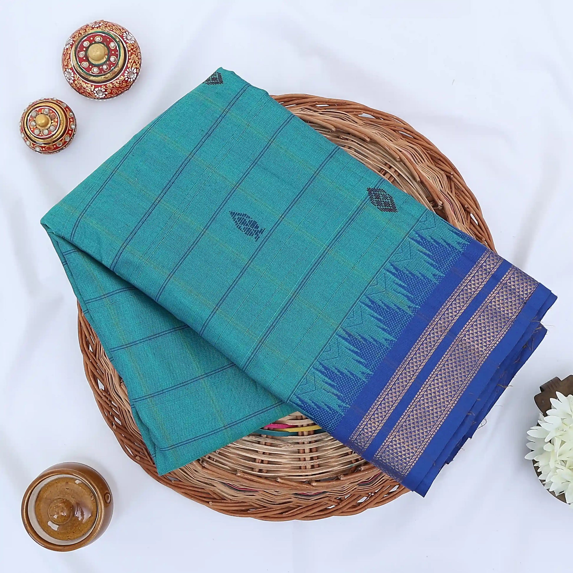 Chettinad cotton saree with teal striped body blue temple zari border and black butta motifs folded flat lay view