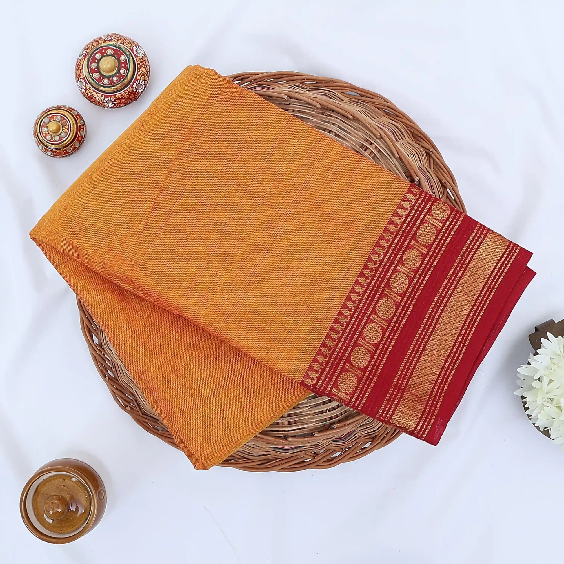 Chettinad cotton saree with plain body and red zari woven border in orange folded top view