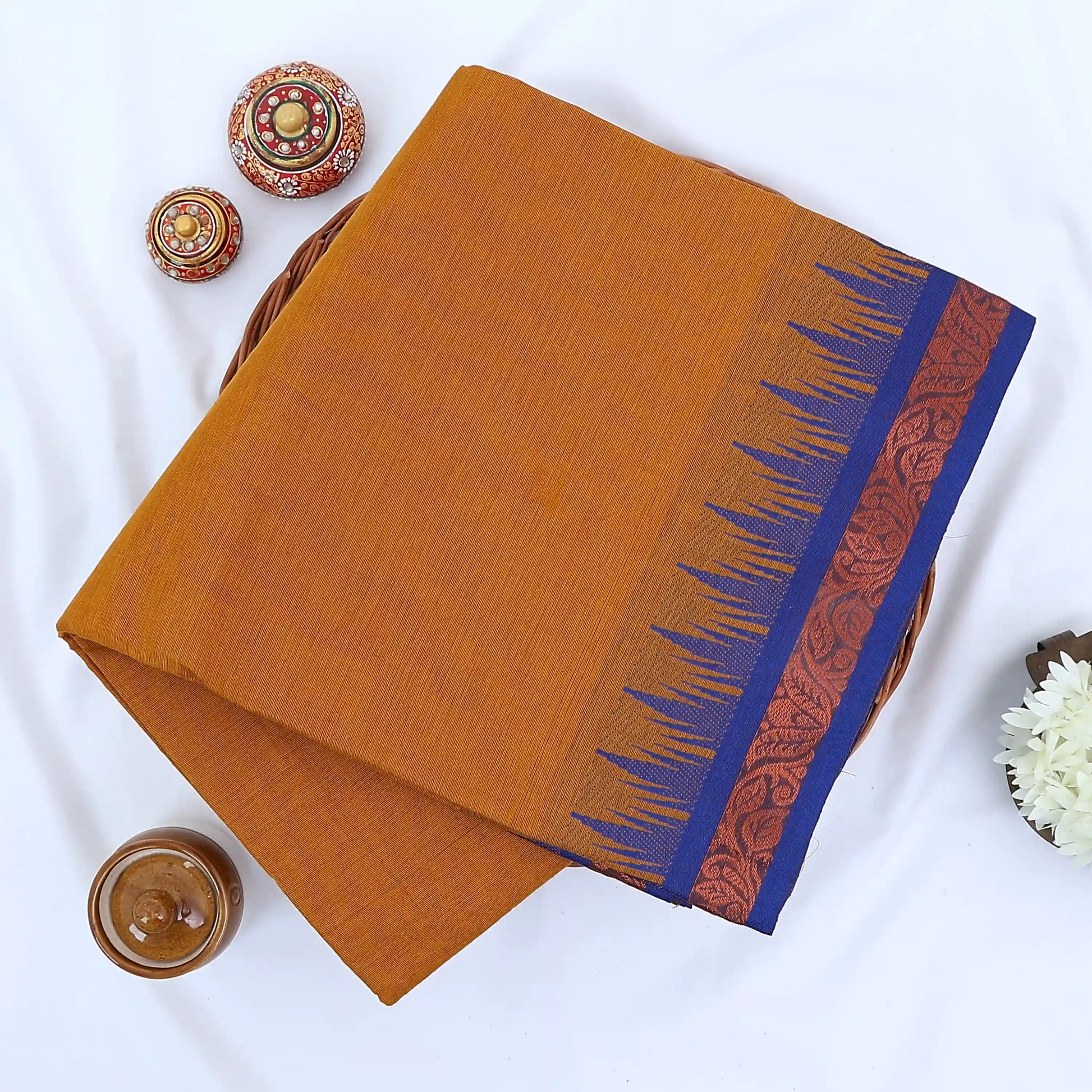 Chettinad cotton saree with plain mustard yellow body blue temple border folded top view on wicker basket