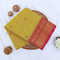 Chettinad cotton saree with yellow body pink buttas and gold zari border folded in a basket top view.