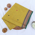 Chettinad cotton saree with yellow body buttas and grey peacock zari border folded in a basket top view.