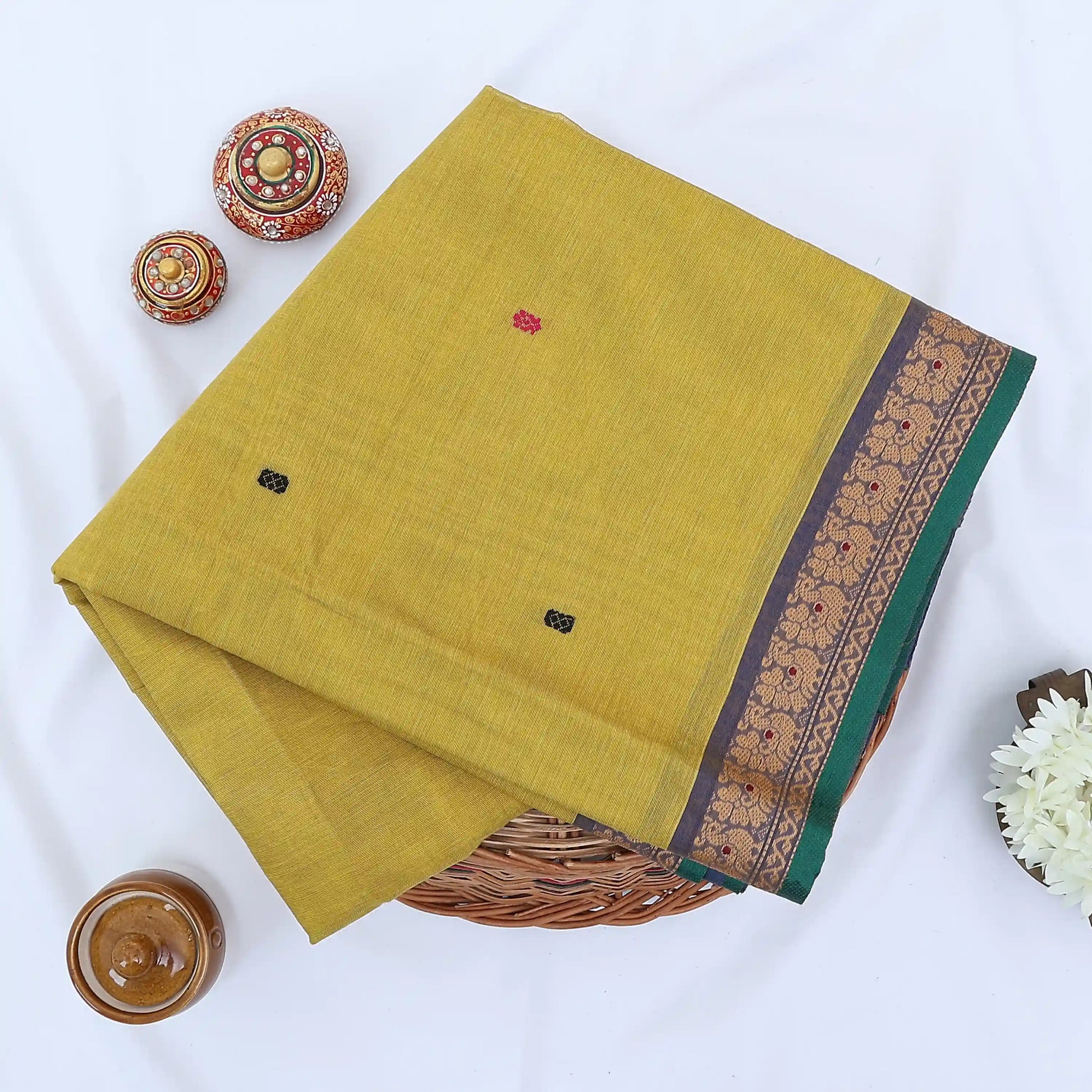 Chettinad cotton saree with yellow body buttas and grey peacock zari border folded in a basket top view.