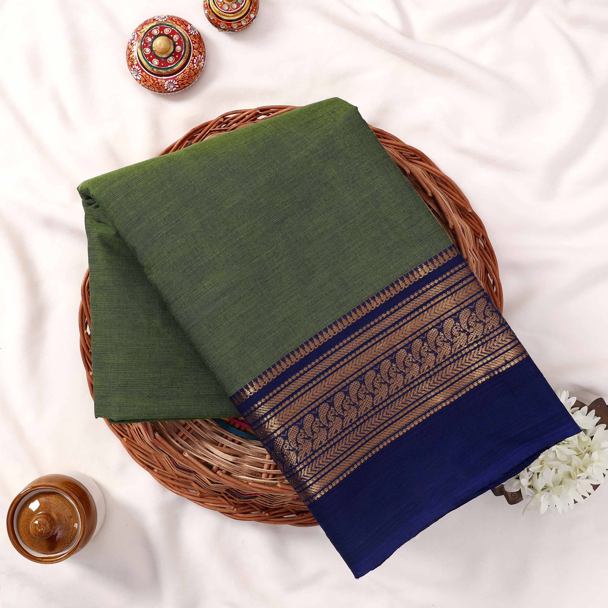Kanchi Cotton Saree With Green Body And Royal Blue Zari Border Folded Flat Lay View On Wicker Tray
