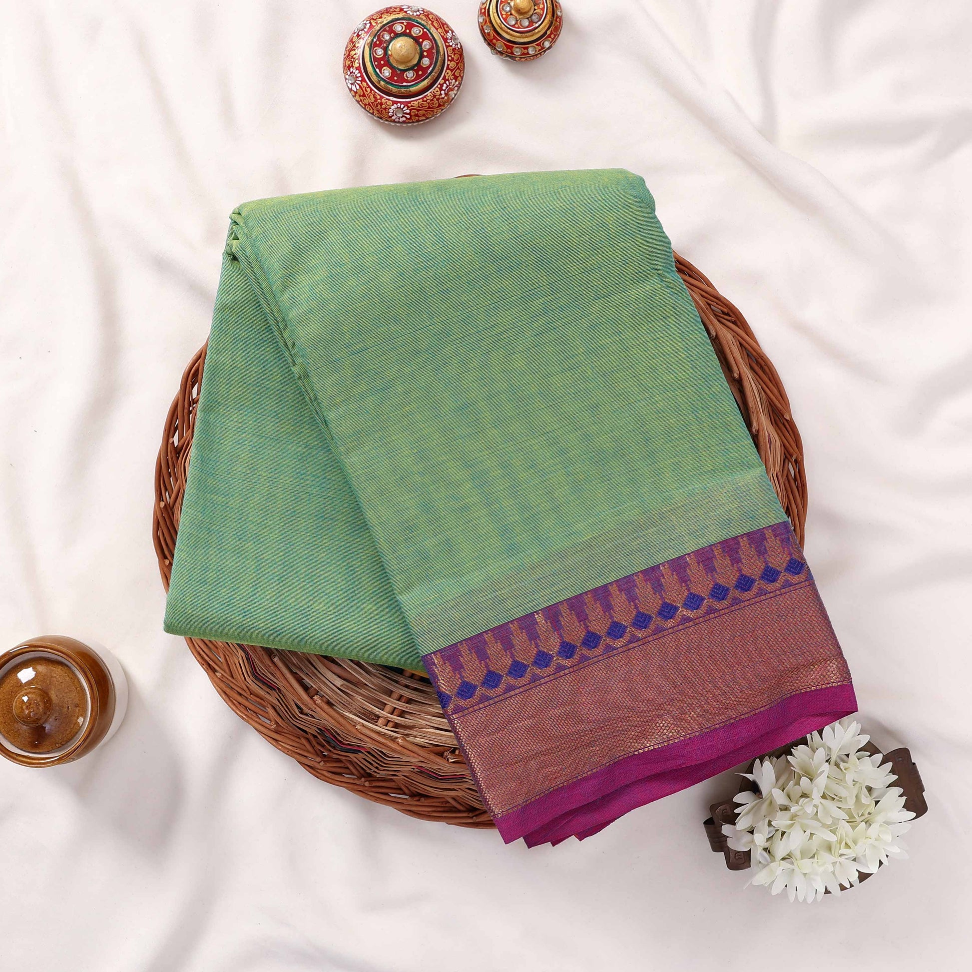 Kanchi Cotton Saree In Light Green With Purple And Gold Zari Border Folded Display Top View With Decorative Accents
