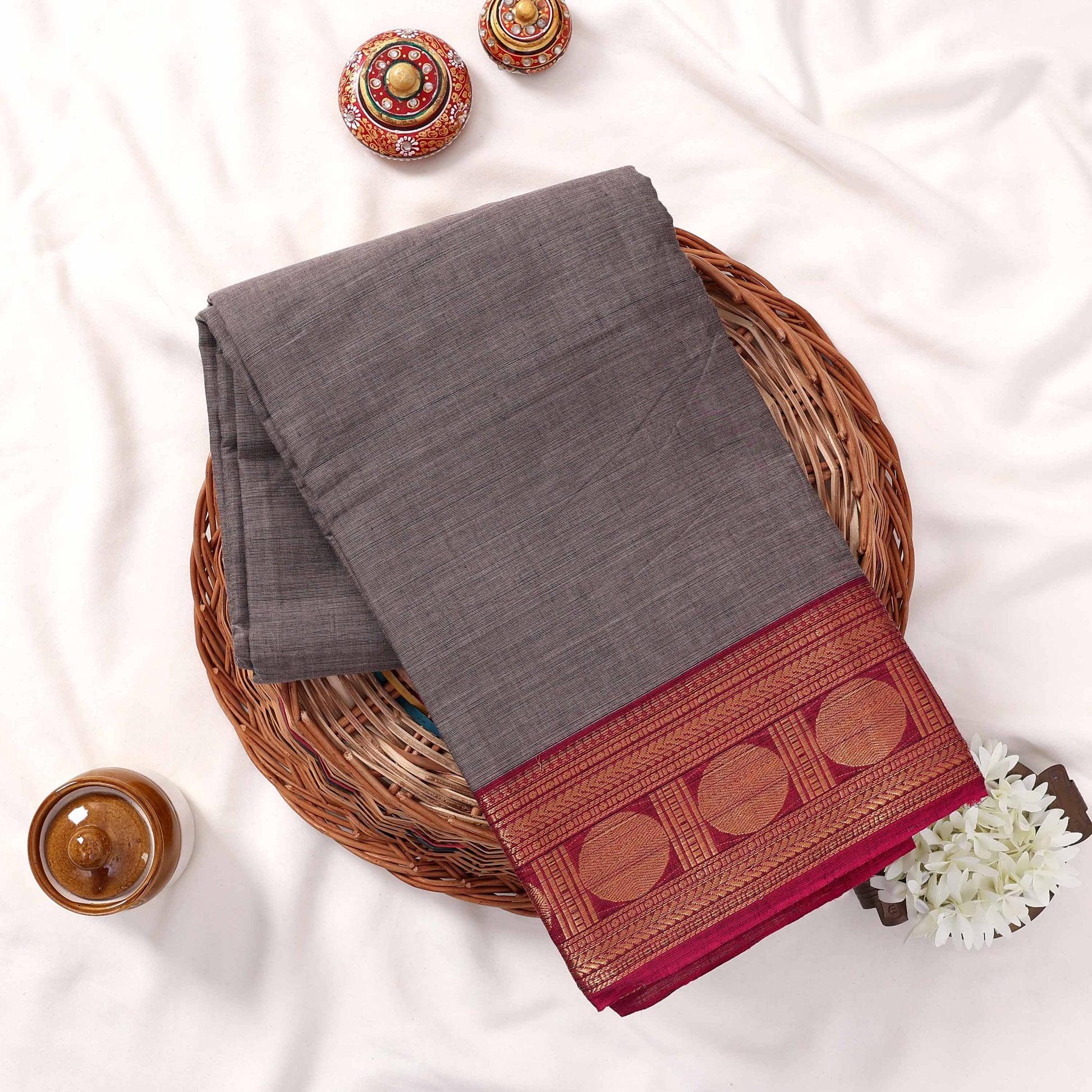 Kanchi Cotton Saree With Solid Grey Weave And Maroon Zari Border Neatly Folded Flat Lay View With Decorative Accents
